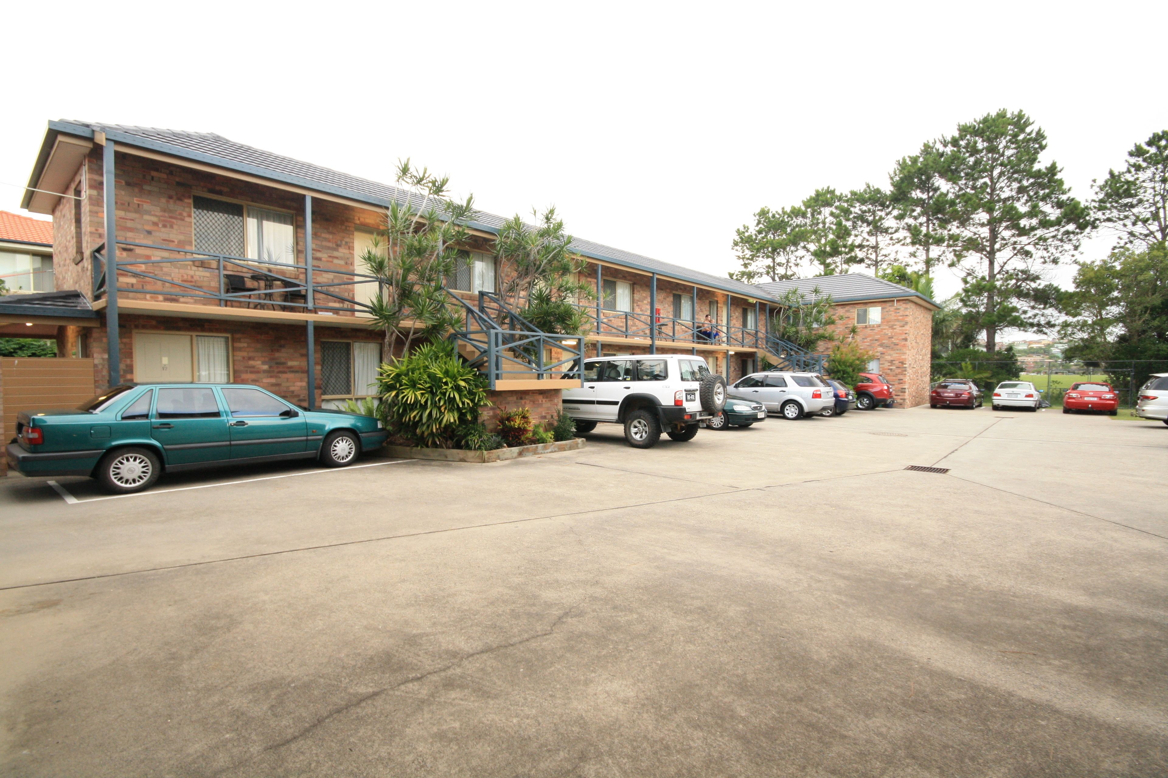 A motel with a brick facade, multiple parking spaces, and a small garden area.