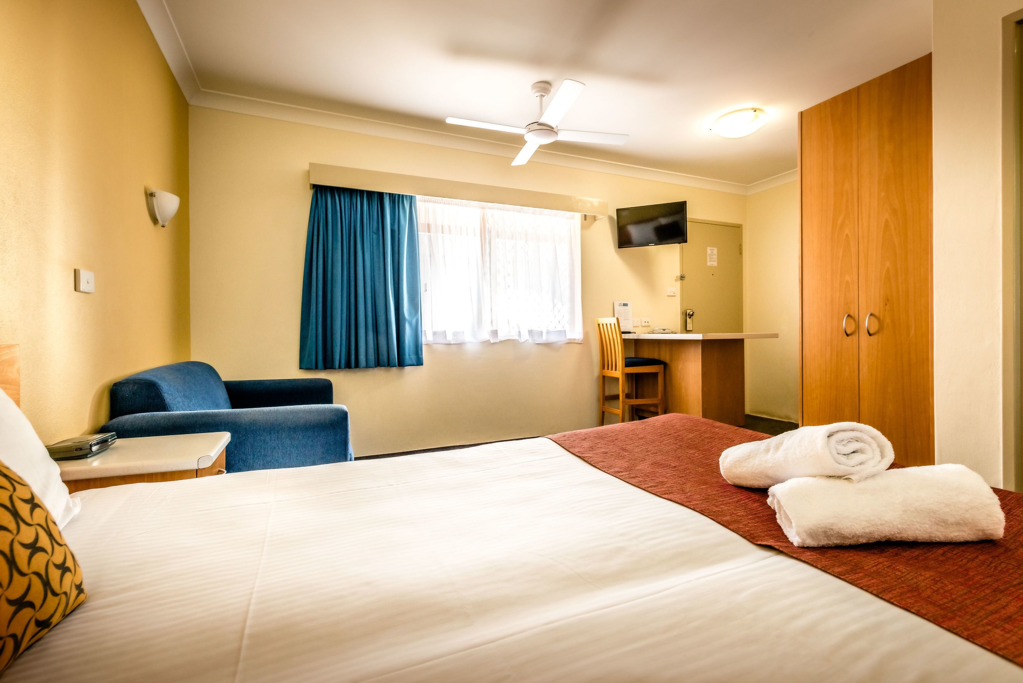 Una habitación de hotel con cama, escritorio, silla, televisión y armario.