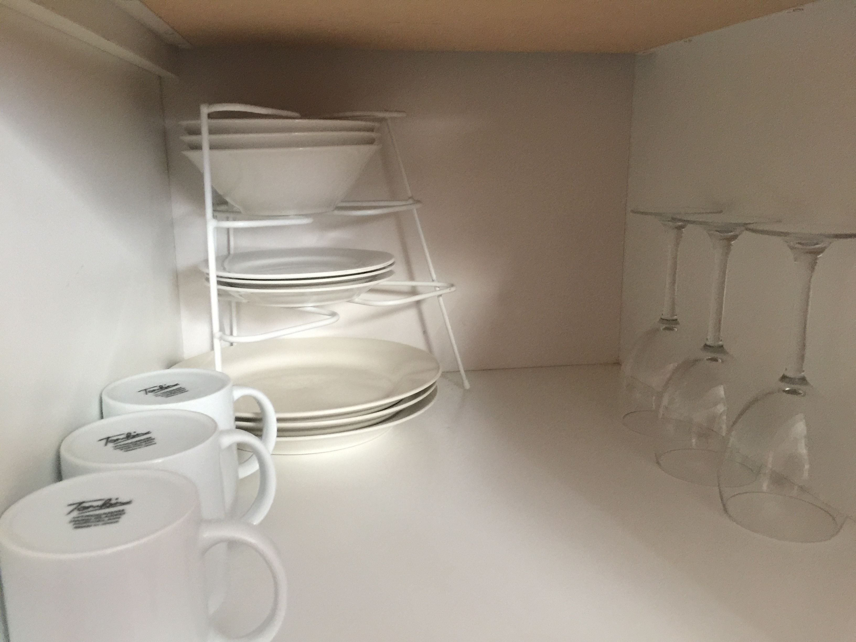 A white shelf with plates, bowls, and mugs, and a wine rack with glasses.