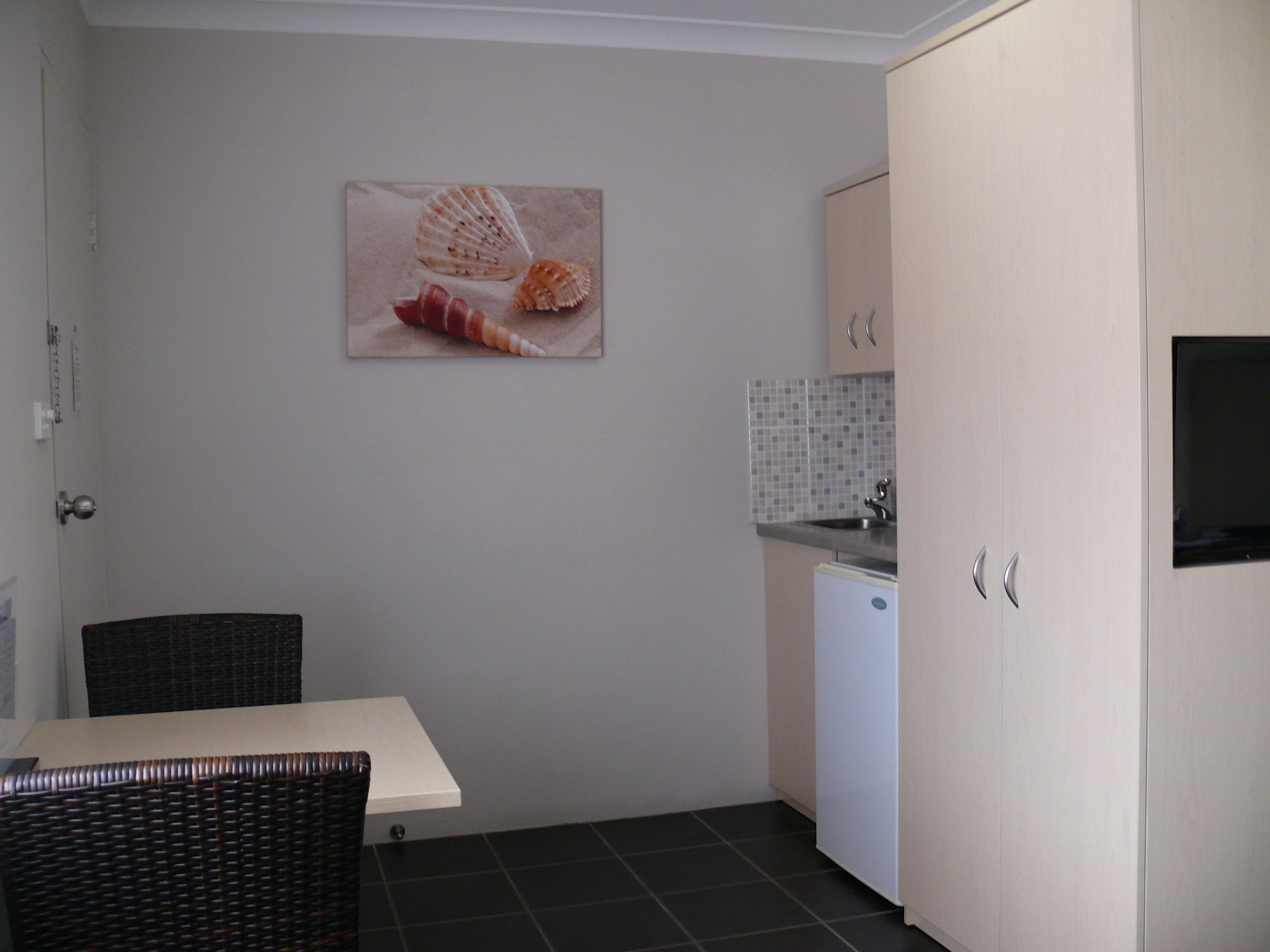 A compact kitchen with a dining area, a small refrigerator, and a wall-mounted picture of seashells.