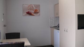 A compact kitchen with a dining area, a small refrigerator, and a wall-mounted picture of seashells.