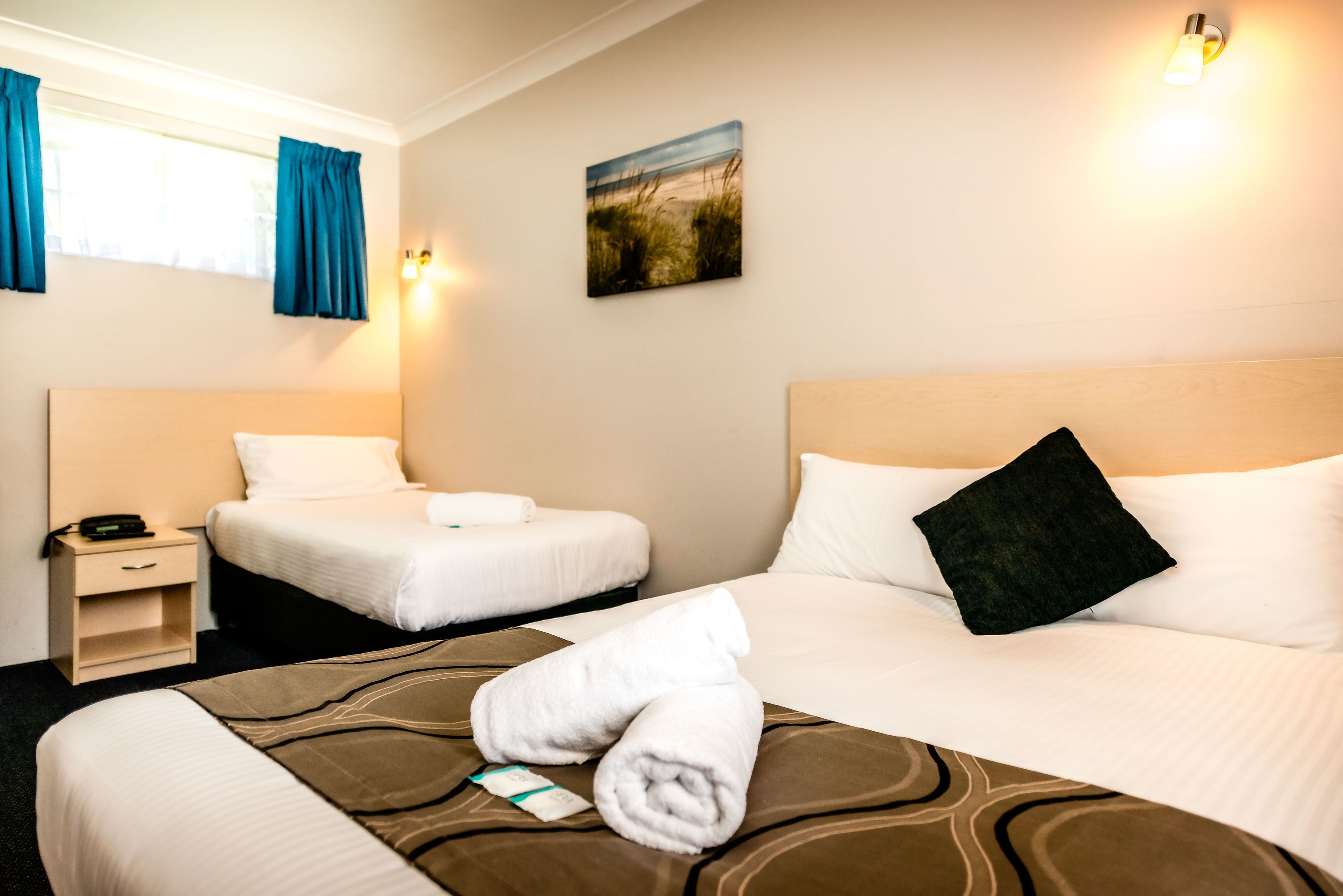 Habitación de hotel con dos camas, una mesita de noche, un cuadro en la pared y una ventana con cortinas.