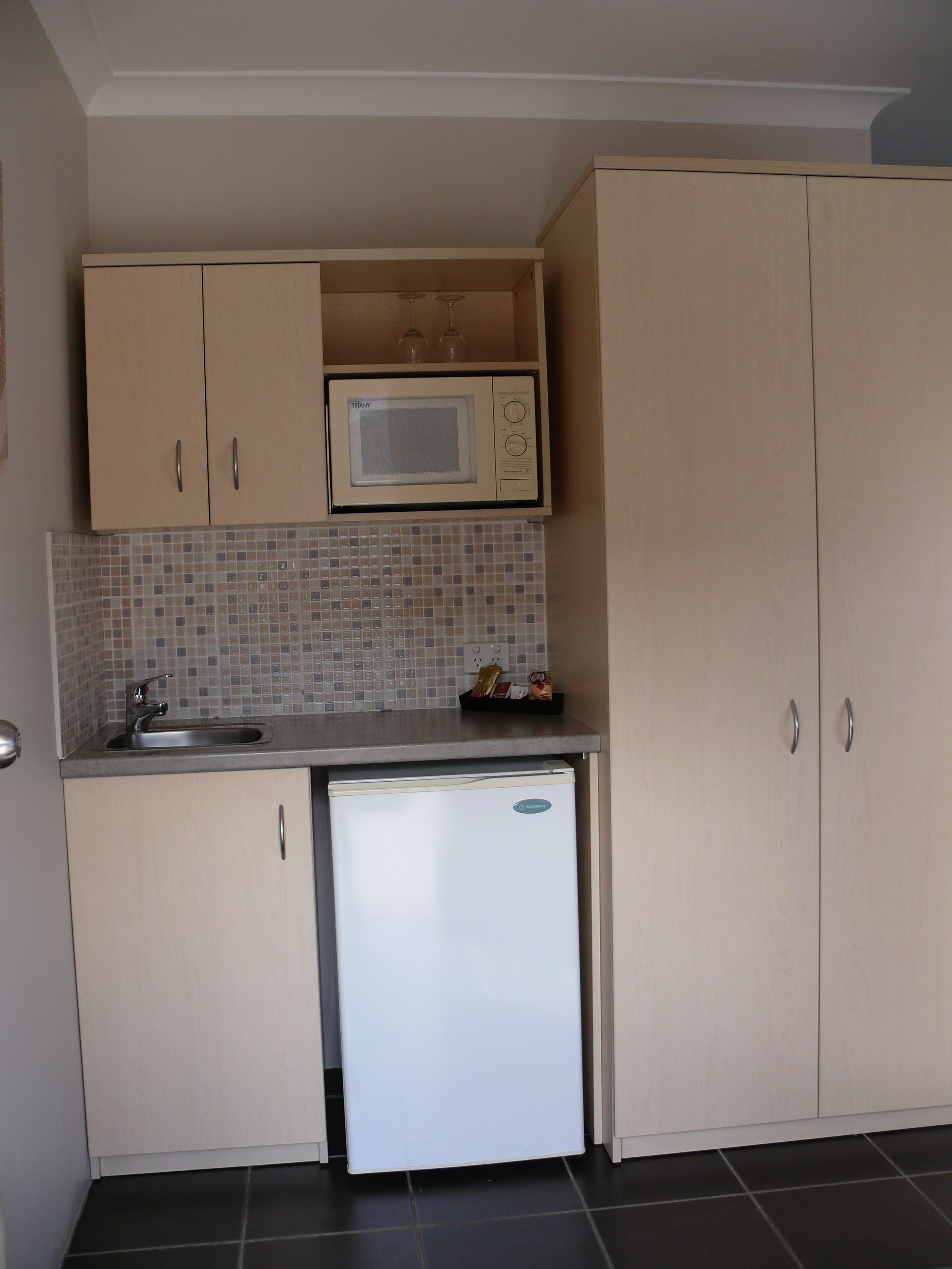 Una cocina compacta con microondas, un refrigerador pequeño y un salpicadero de azulejos.