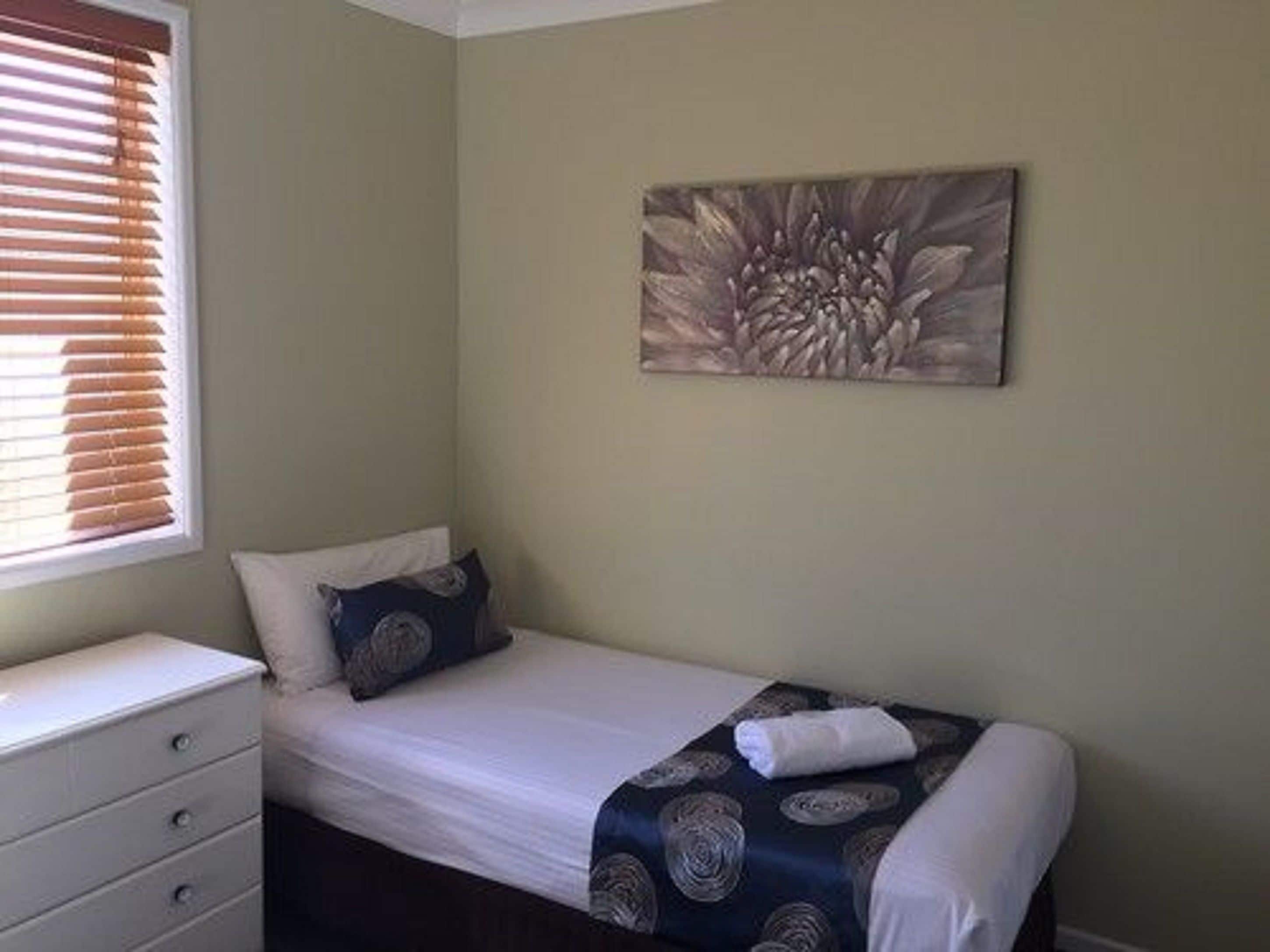 A bedroom with a bed, a dresser, and a window with blinds.