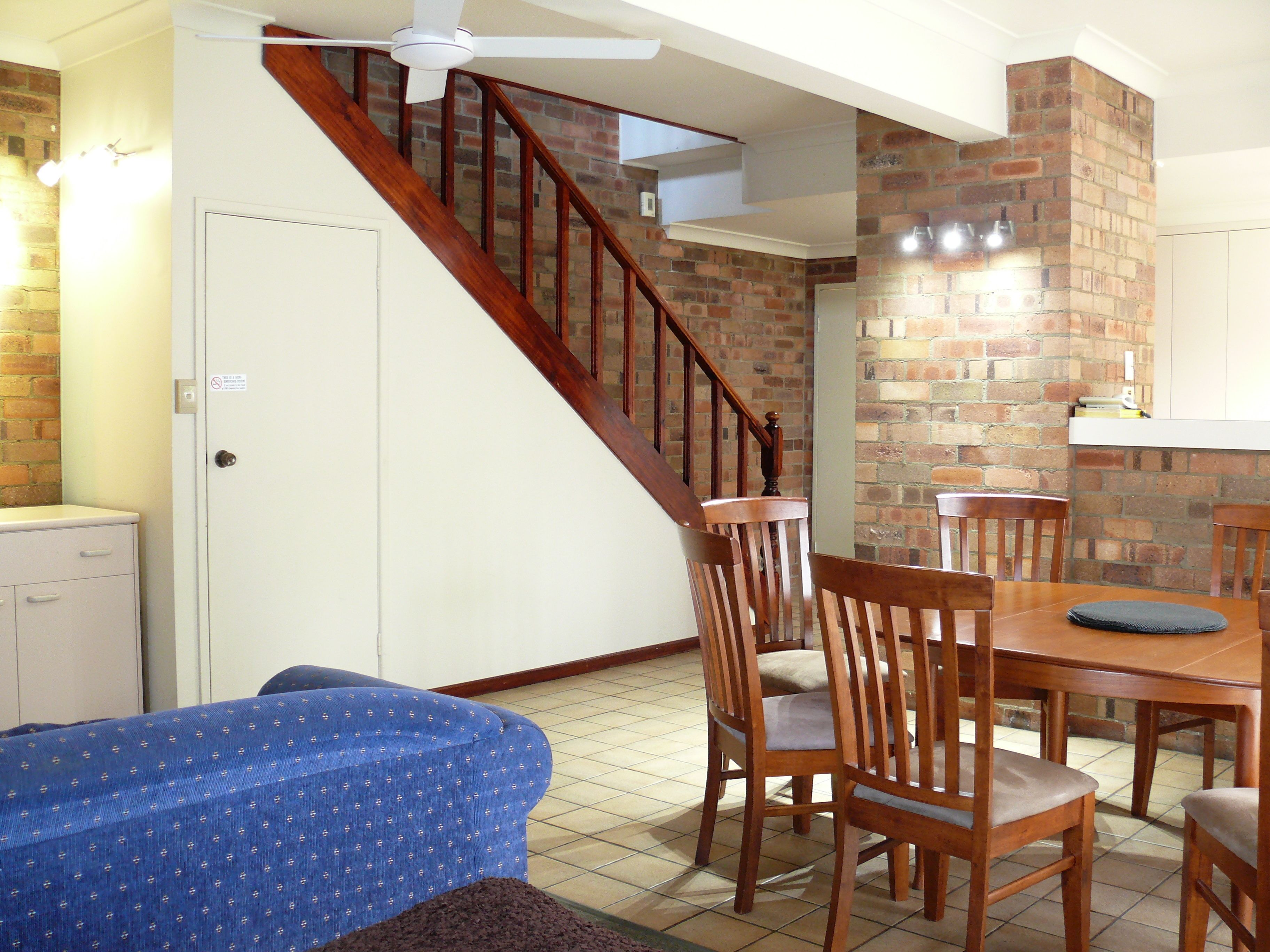 Un coin repas avec une table et des chaises en bois, un canapé bleu et un escalier avec un mur en briques.