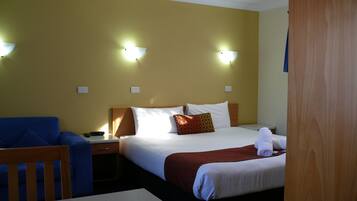 A hotel room with a bed, a desk, and a chair. There are two wall-mounted lights and a door.