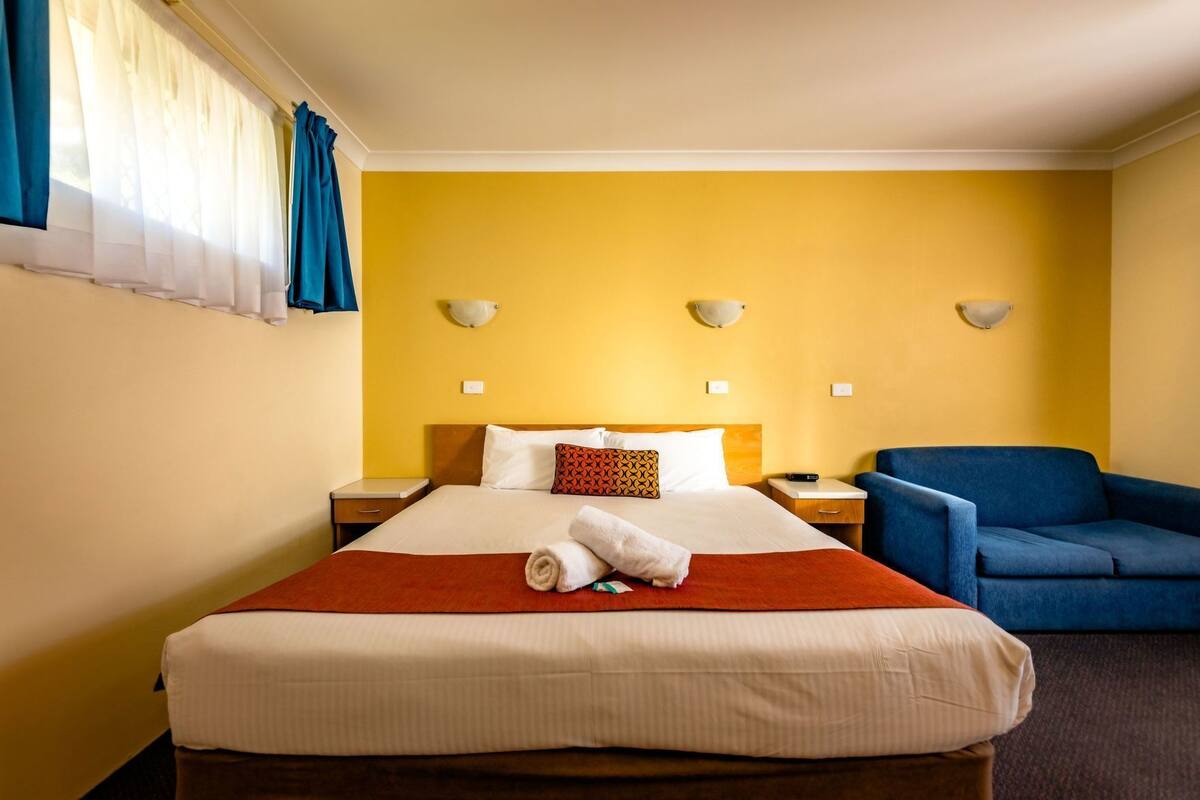 A hotel room with a bed, bedside tables, a blue armchair, and wall-mounted lamps.