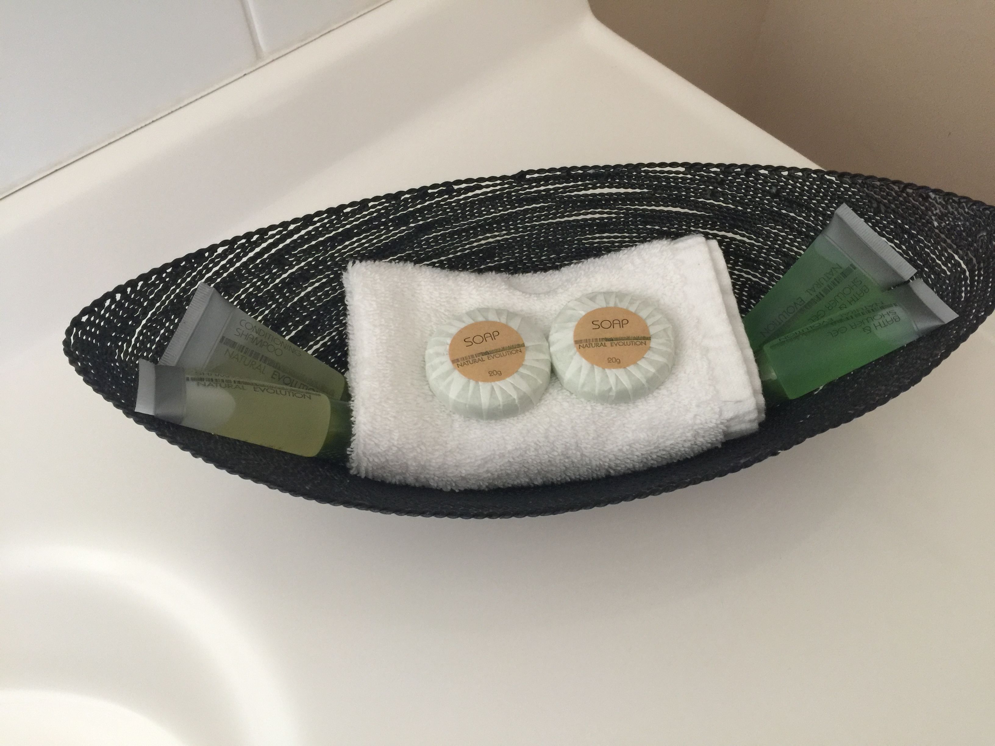 A black woven basket containing two soap bars and a green bottle, placed on a white surface.
