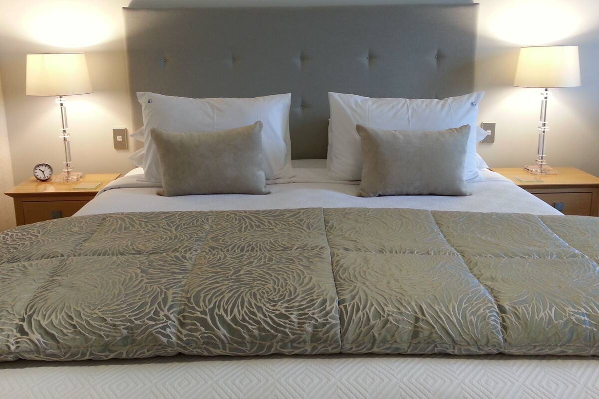 A neatly made bed with a patterned bedspread, two bedside lamps, and a clock on the nightstand.