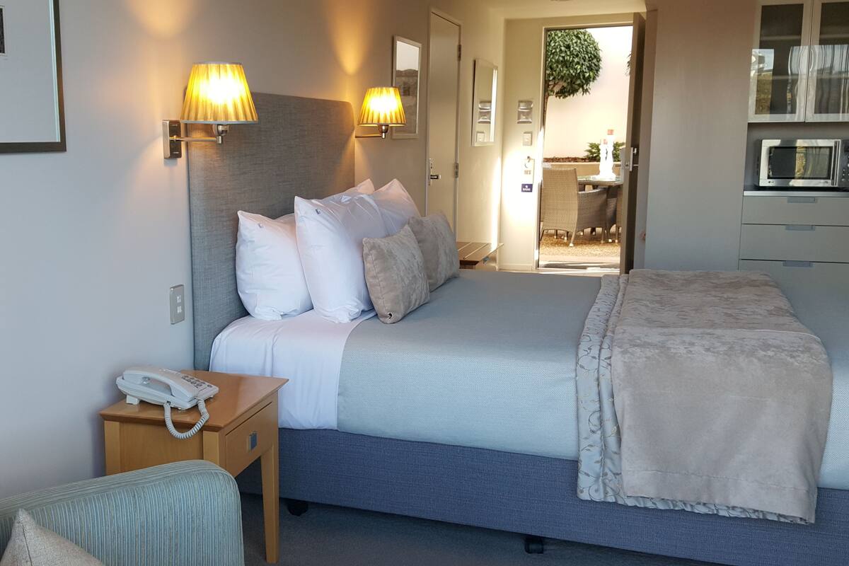 A hotel room with a bed, bedside lamps, a telephone, a small table, and a view of the outside.