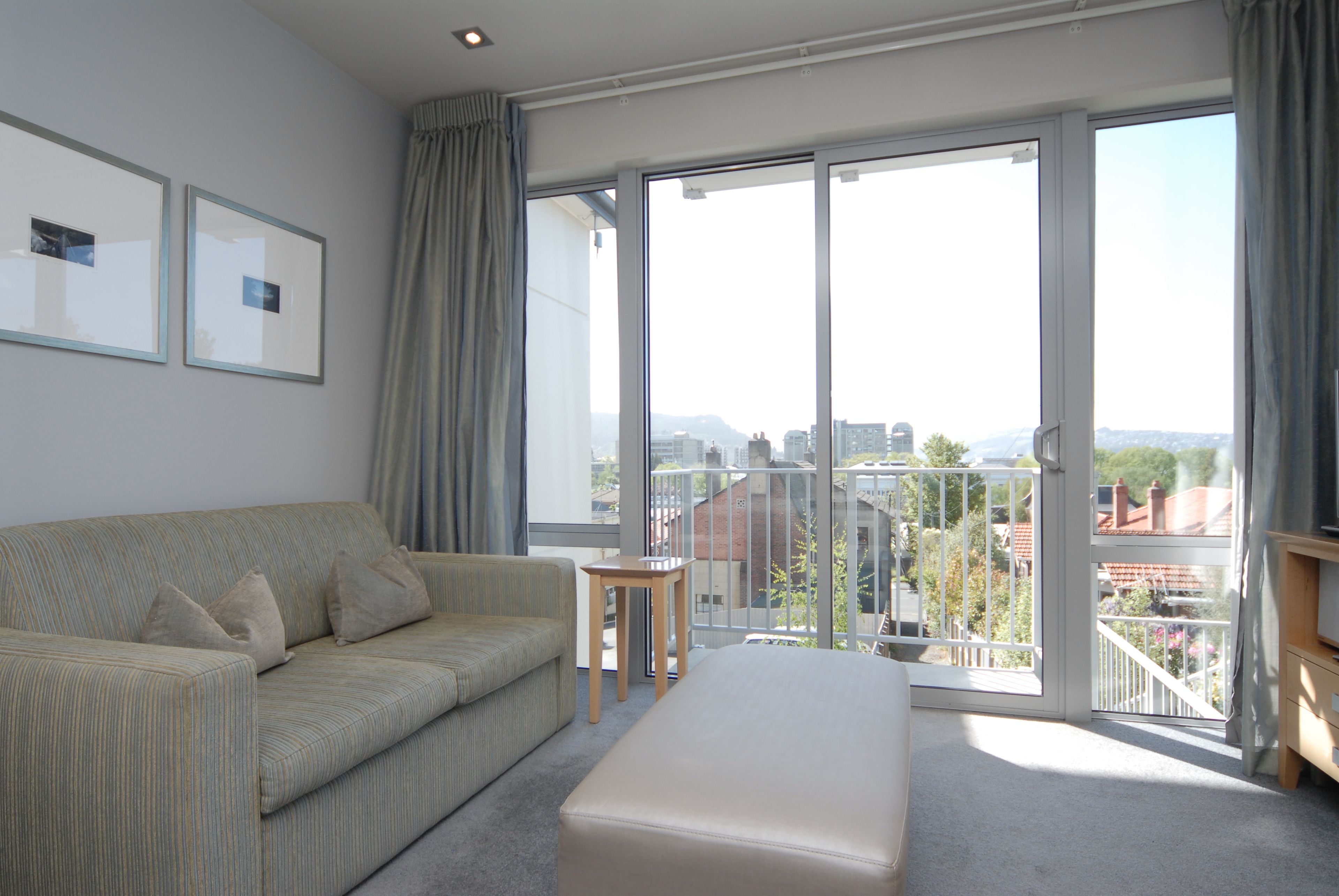 A modern hotel room with a large balcony, a sofa, a small table, and a bed.
