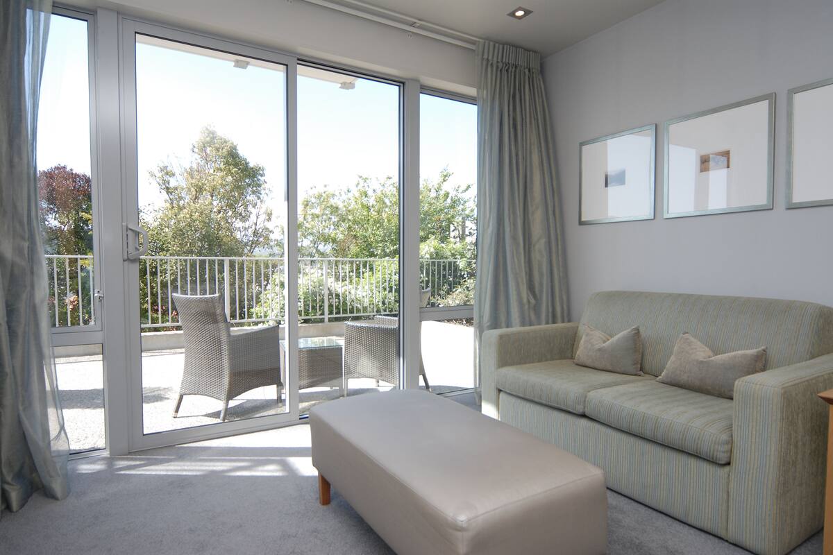 A spacious living room with a sofa, a bench, and a balcony with outdoor furniture.