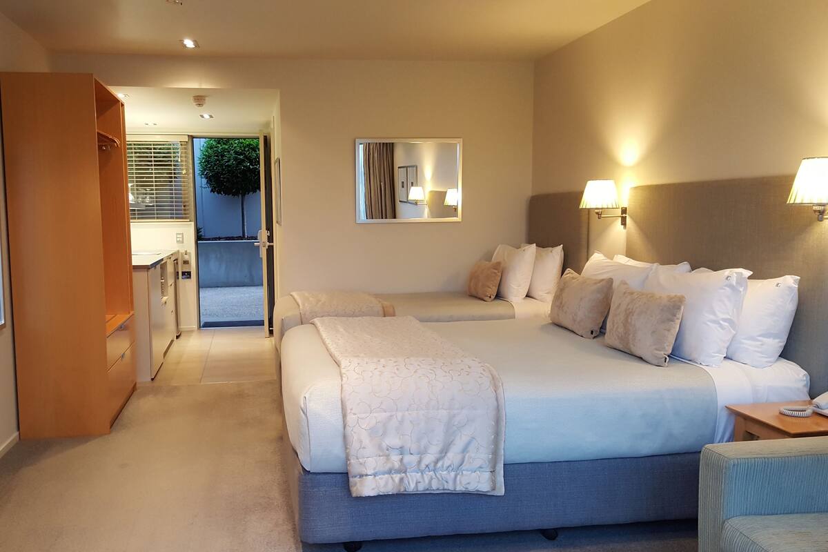 A hotel room with a large bed, bedside tables, a wardrobe, and a view into the kitchen area.