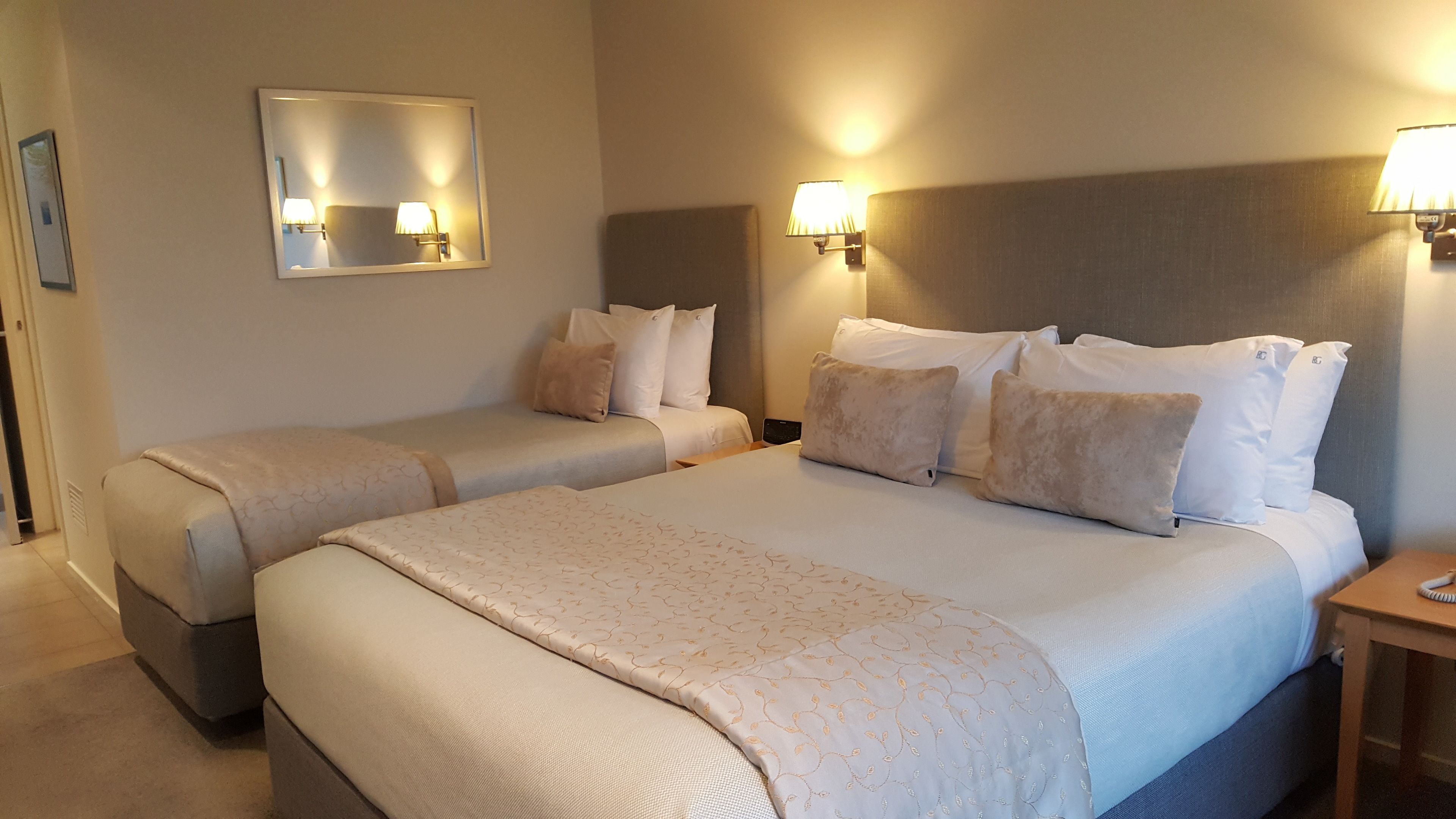 Une chambre d’hôtel avec deux lits, un grand miroir, des lampes de chevet et une table de chevet.