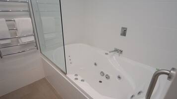 Une salle de bain moderne avec une douche à parois de verre, une baignoire blanche dotée de plusieurs robinets et un porte-serviettes en métal.