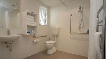 A bathroom with a sink, toilet, shower, and a window with blinds.