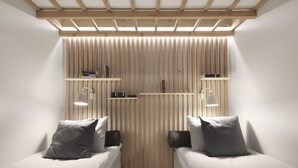Un dormitorio con dos camas individuales, paredes de listones de madera y estanterías empotradas con libros y objetos decorativos.