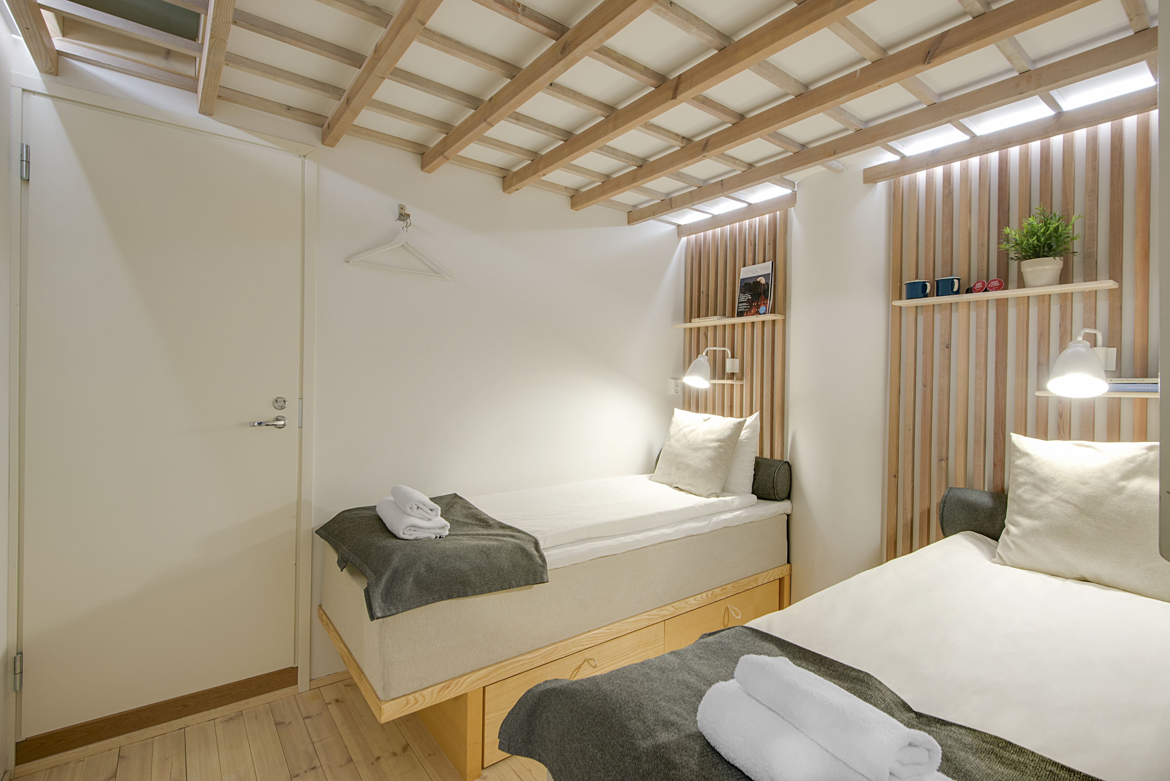 Un dormitorio con dos camas, un armario, una lámpara colgante, una estantería con adornos y un techo de madera.