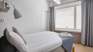 A bedroom with a bed, a bedside lamp, a window with curtains, and a radiator.