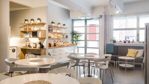 Una cocina moderna con encimeras blancas, estantes empotrados y una zona de comedor con mesas y sillas redondas.