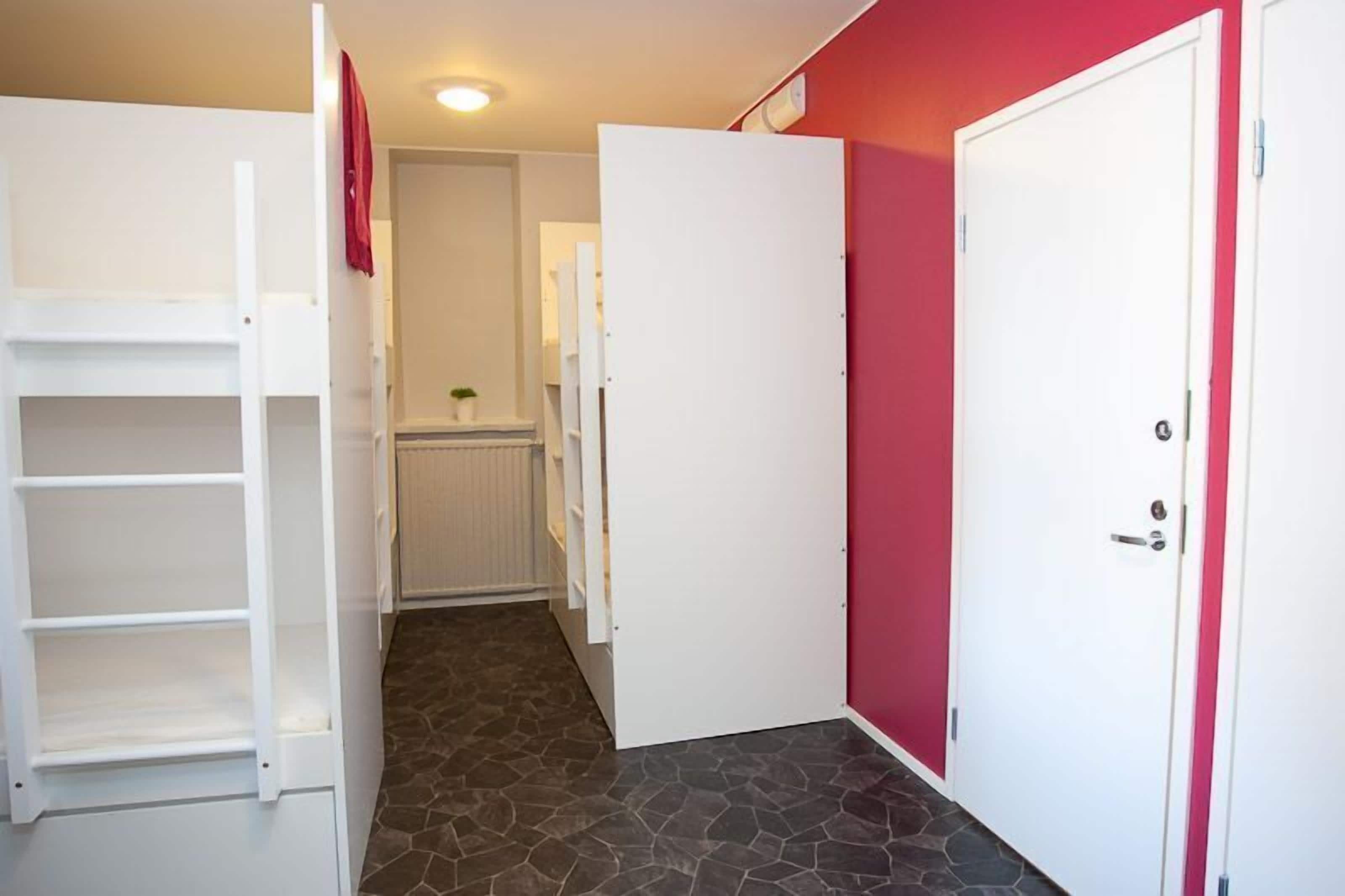 A narrow hallway with a white wardrobe, a red wall, and a white door.