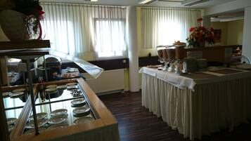 Dispositiu de bufet amb diversos plats i una estació de begudes, un arranjament floral i una finestra amb cortines.