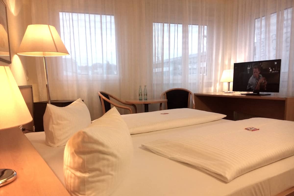 A hotel room with a bed, a desk, a chair, a TV, and a lamp.