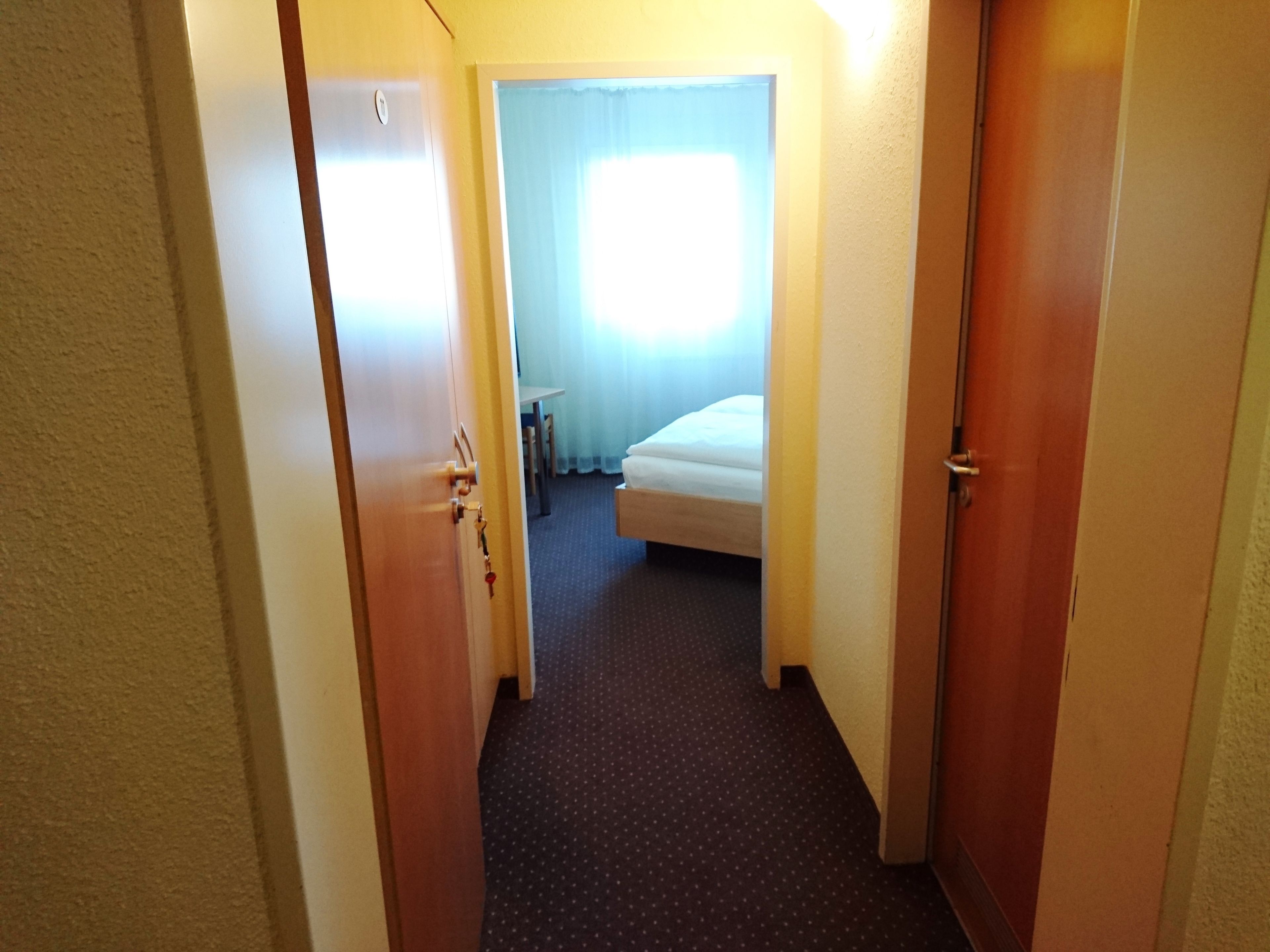 Um corredor estreito que leva a um quarto com cama e janela.