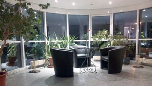 A modern indoor seating area with a glass table and chairs, surrounded by large windows and potted plants. - Central Hotel (Winnenden)