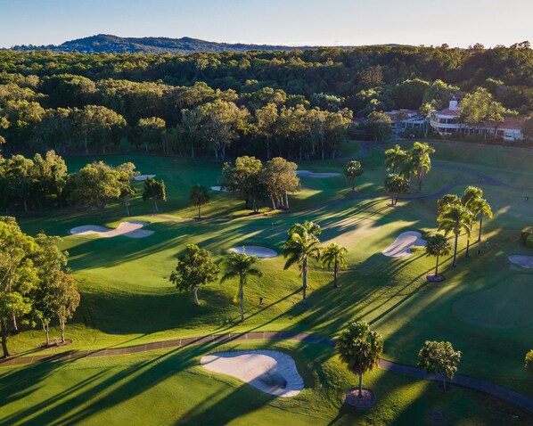 An aerial view of a golf course with sand bunkers, palm trees, and a clubhouse in the distance. - Noosa Springs Golf Resort & Spa (Noosa Heads)