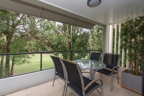 A balcony with a glass table and chairs, a view of a grassy area, and a potted plant. - Noosa Springs Golf Resort & Spa (Noosa Heads)