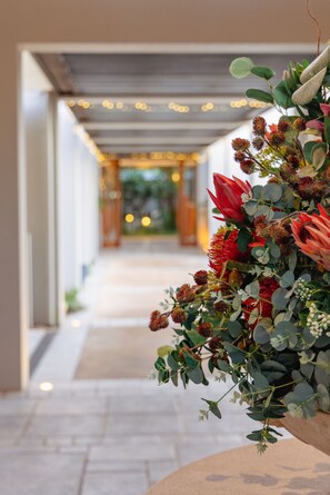 A corridor with a floral arrangement on the right, leading to a warmly lit area with string lights. - Noosa Springs Golf Resort & Spa (Noosa Heads)