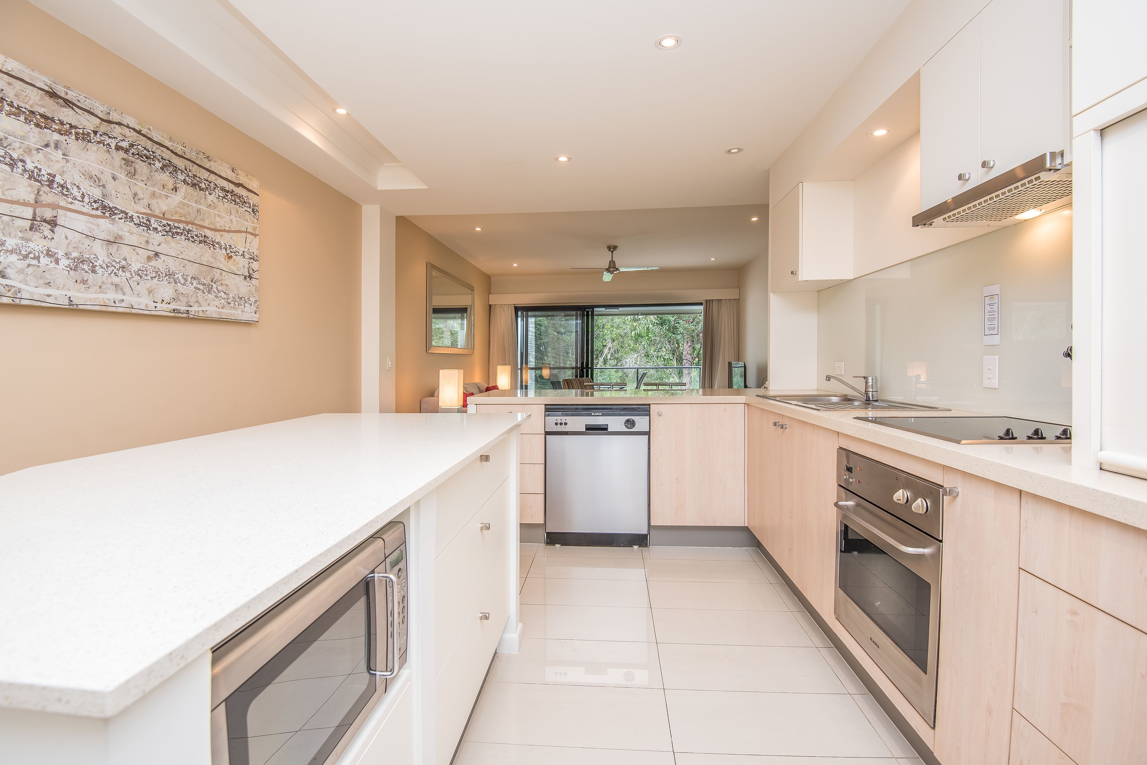 Een moderne keuken met witte kastjes, roestvrijstalen apparatuur en een groot raam met uitzicht op de omgeving.