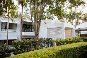 A modern building with white exterior walls, multiple balconies, and lush greenery including palm trees and well-maintained hedges. - Noosa Springs Golf Resort & Spa (Noosa Heads)