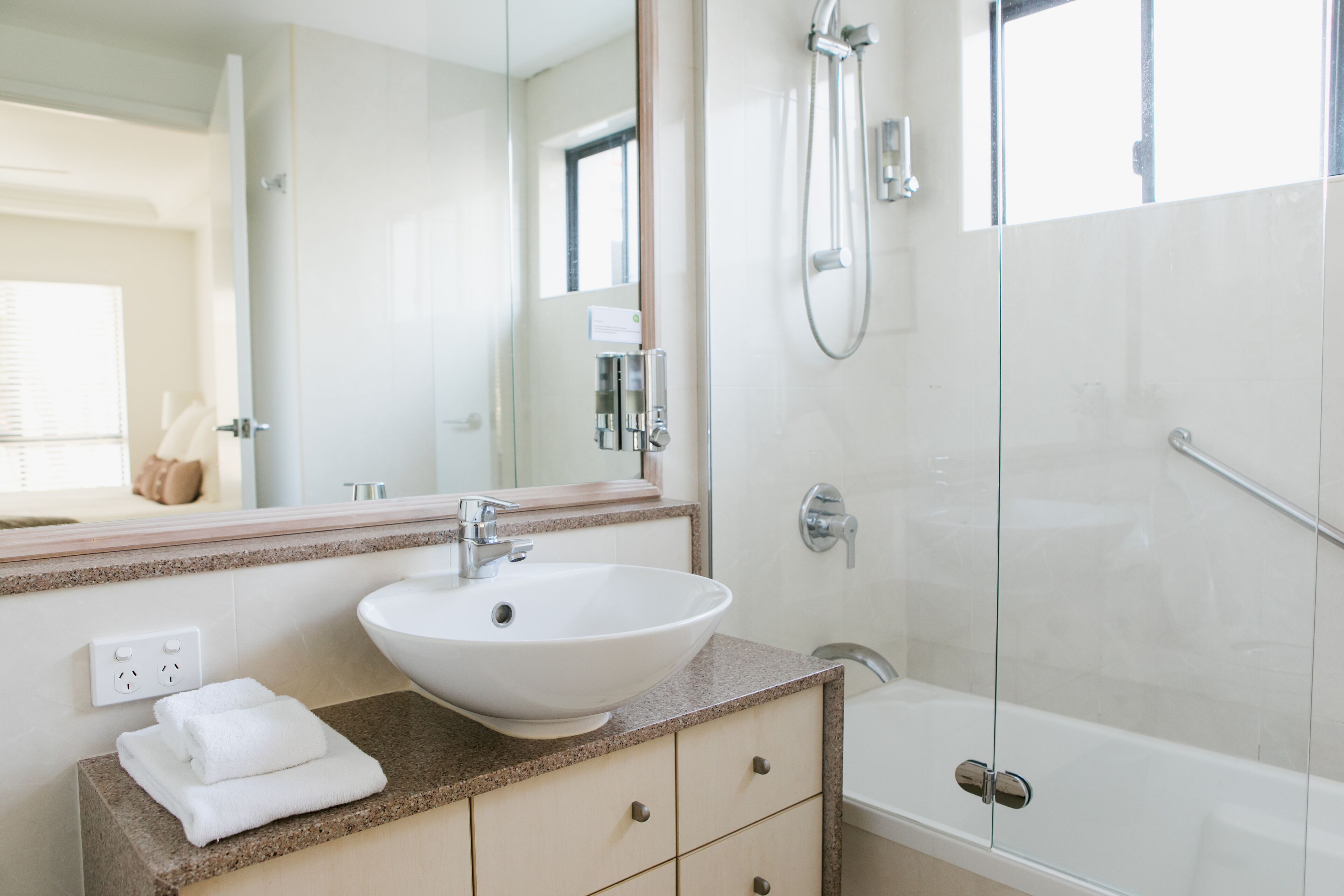 Un baño moderno con un lavamanos blanco, mampara de ducha de vidrio y un espejo grande.