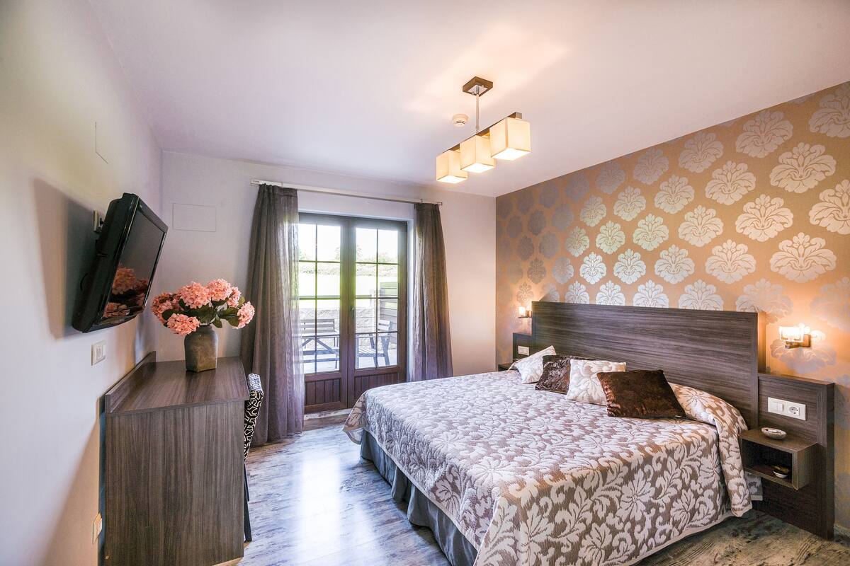 A bedroom with a large bed, a dresser, a TV, and a window with curtains.