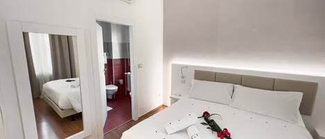 A hotel room with a bed, a bedside table, a nightstand, a mirror, and an air conditioning unit.