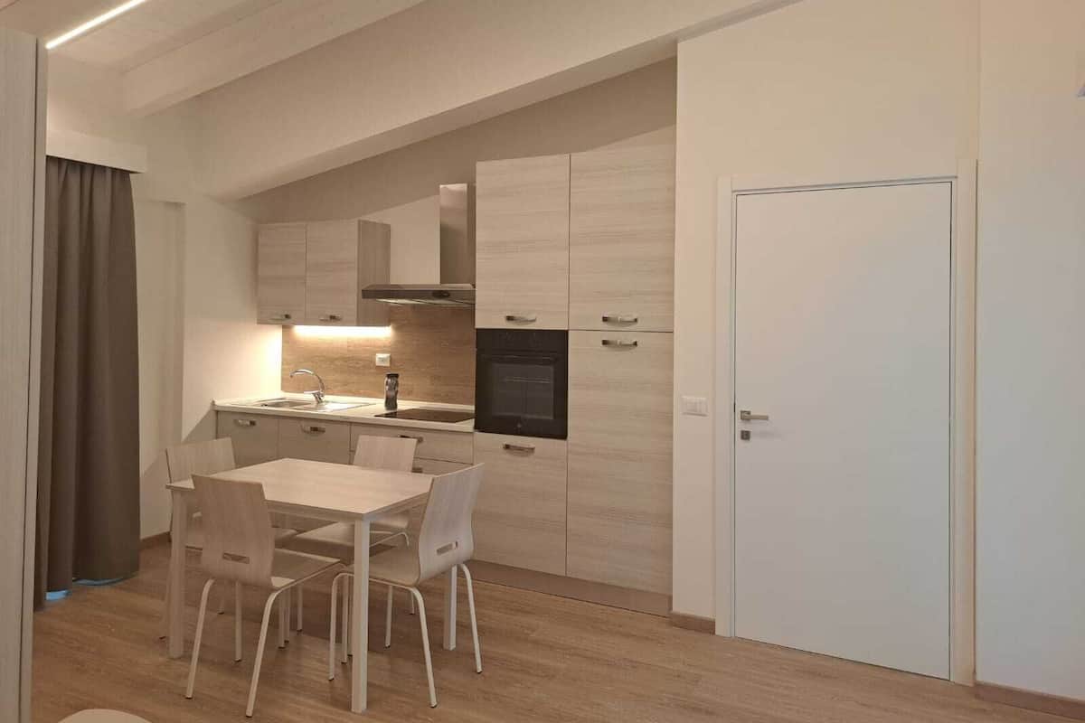 A modern kitchen with light wood cabinetry, a built-in oven, and a dining area with a table and chairs.