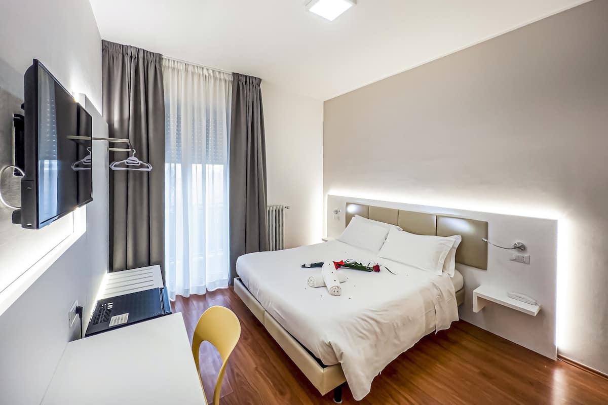 A modern hotel room with a bed, bedside table, and a TV mounted on the wall.