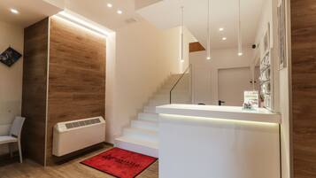 A modern hotel lobby with a wooden accent wall, a reception desk, a staircase, and a red doormat.