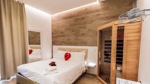 Una cama bien hecha con un adorno con forma de corazón, un armario de madera y una mesita de noche con una lámpara.