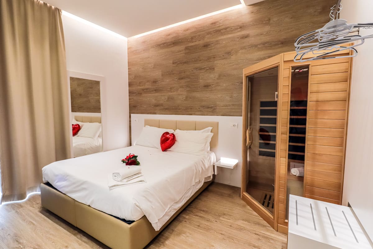 A neatly made bed with a heart-shaped decoration, a wooden wardrobe, and a bedside table with a lamp.