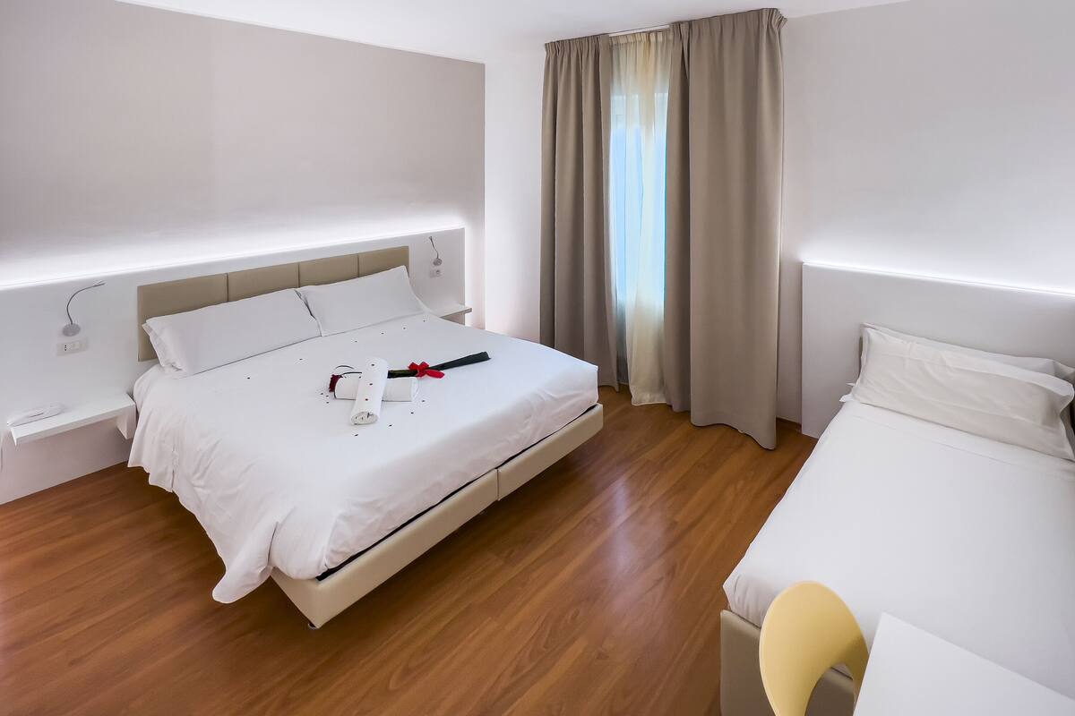 A modern hotel room with a large bed, bedside tables, and a window with curtains.