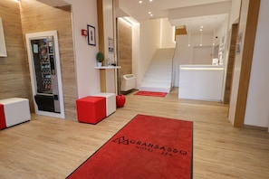 A hotel reception area with a vending machine, a reception desk, and a staircase leading to the upper floor. - Hotel Gran Sasso (Teramo)