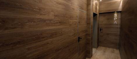 A modern spa room with wooden walls and a glass door leading to a shower area.