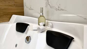 A white bathtub with black bathmats, a bottle of champagne, and a white cup.