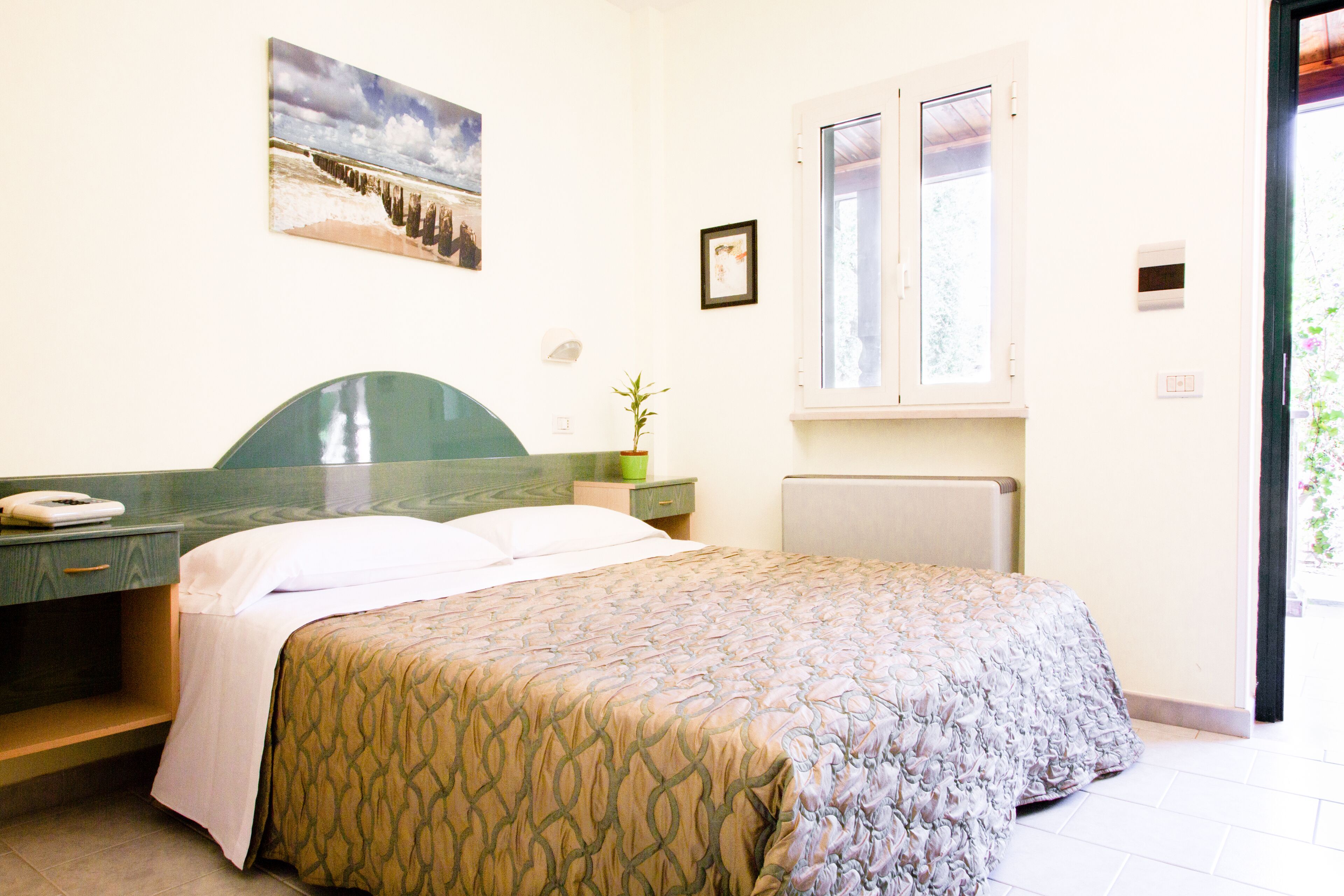 Une chambre d’hôtel avec un lit, une table de chevet, une fenêtre et un tableau au mur.