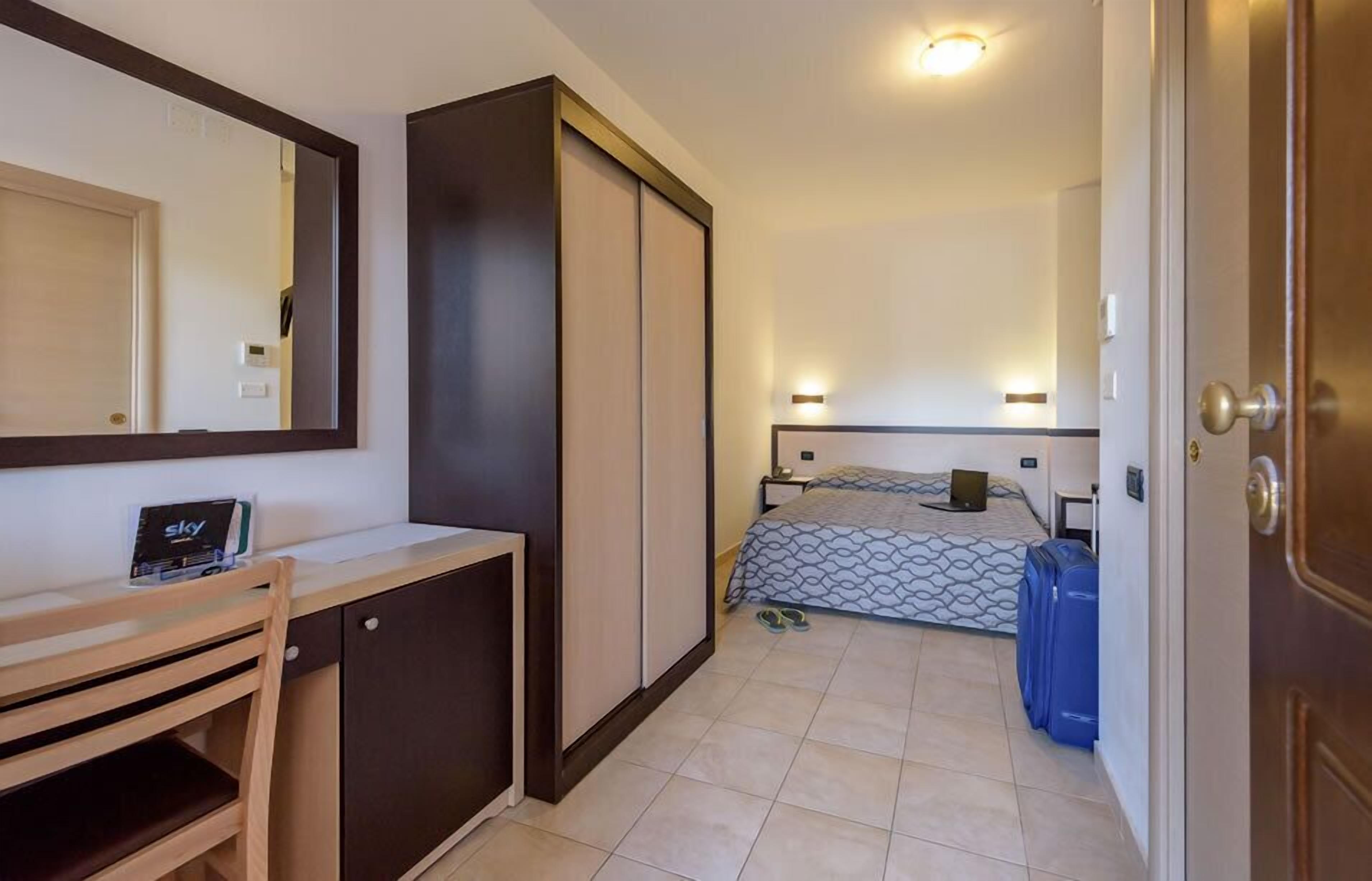 Habitación de hotel pequeña con cama, escritorio, silla, armario y espejo.