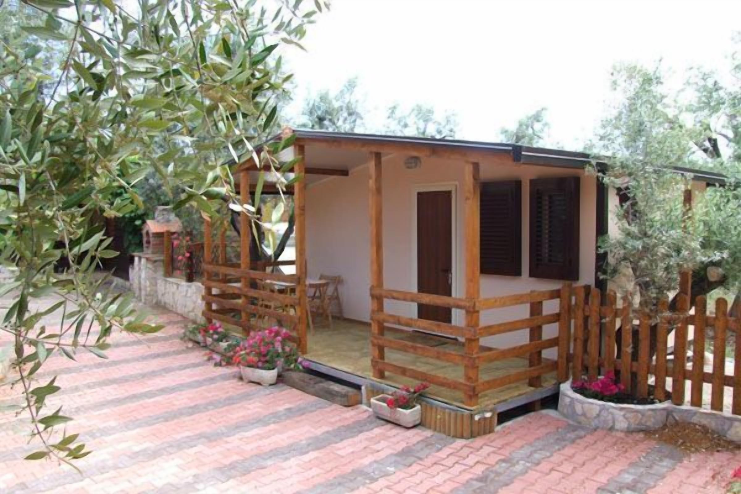 A small wooden cottage with a porch, surrounded by a stone wall and potted plants.