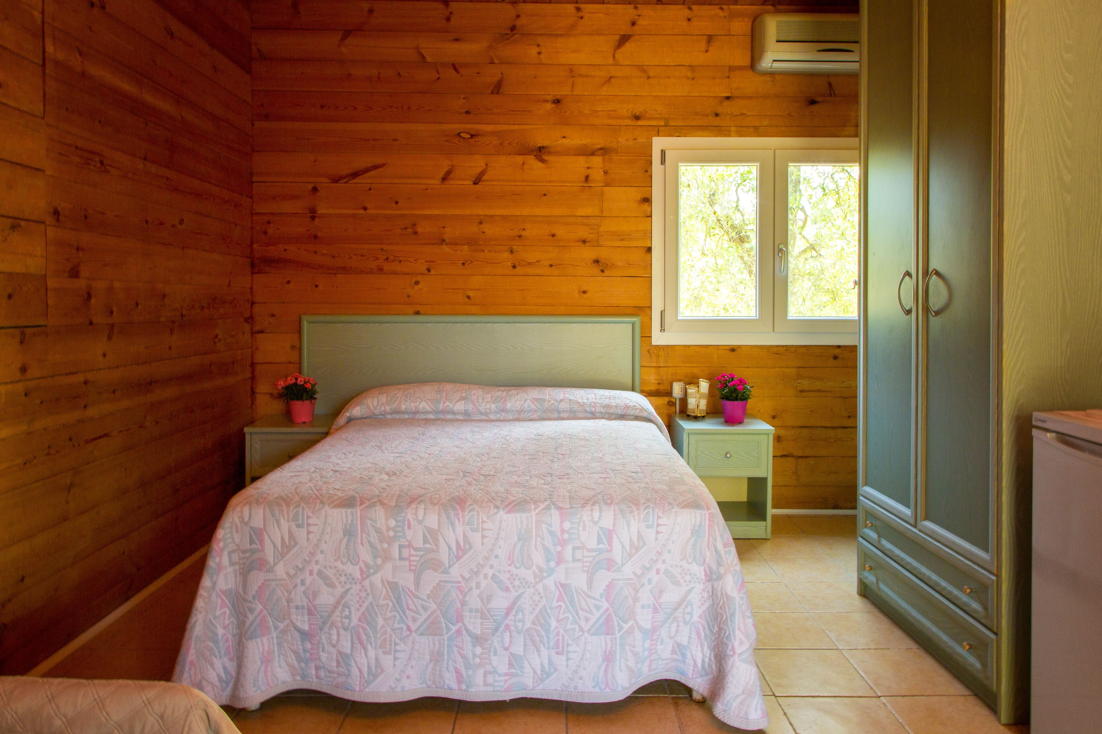 Ein Schlafzimmer einer Holzhütte mit Bett, Nachttischen, einem Schminktisch und einem Fenster.